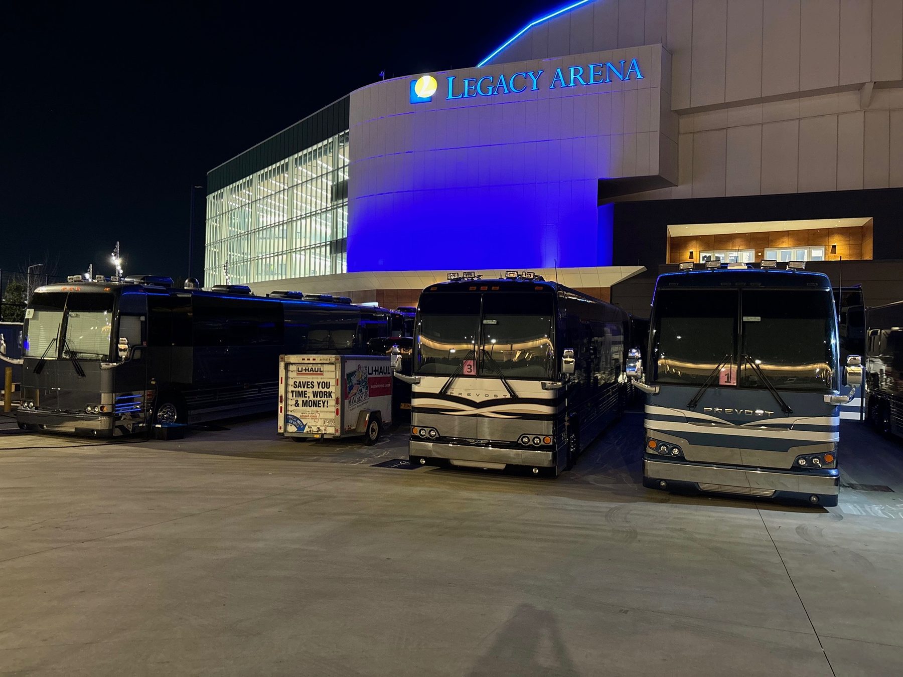 Tour buses staged outside a lit arena